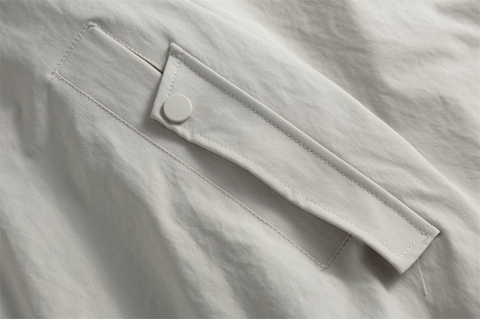 Close-up of a light gray jacket flap with a round snap fastener and stitched edging