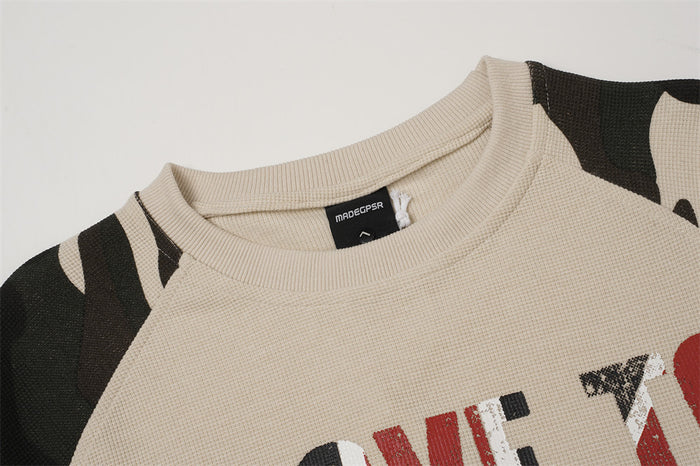 Close-up of the beige shirt's ribbed crew neckline, textured knit fabric, and camouflage raglan shoulder