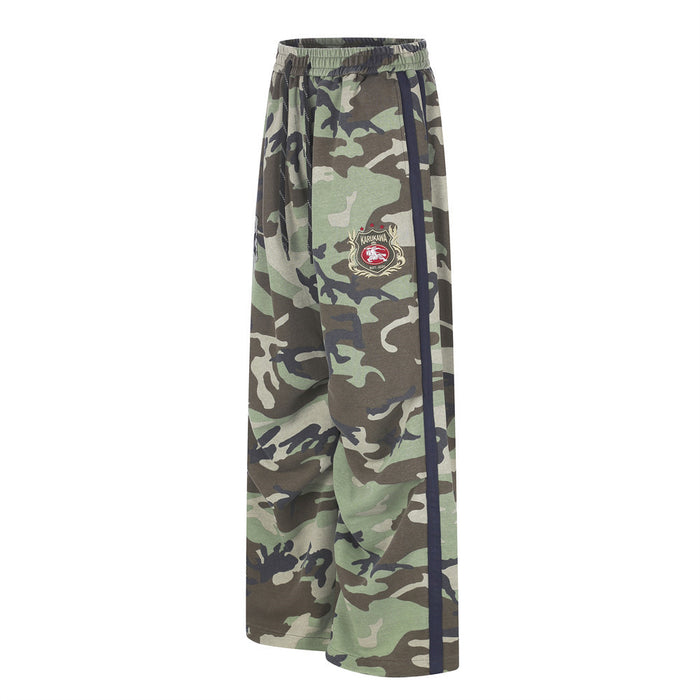 Side view of green and brown camouflage wide-leg sweatpants with navy stripe and crest patch