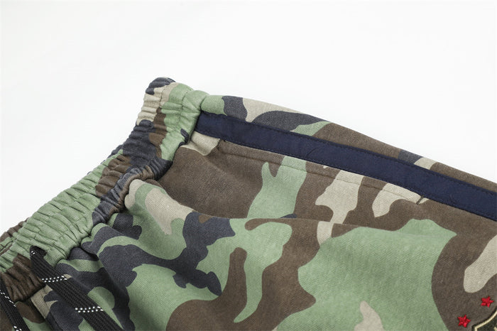 Close-up of camouflage sweatpants waistband and navy side stripe on green and brown fabric