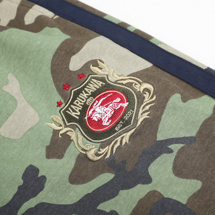 Embroidered crest emblem patch on green and brown camouflage sweatpants beside the navy stripe