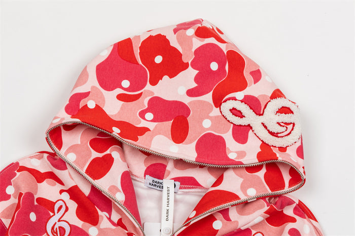 Close-up of a red camouflage hoodie showing the hood, zipper edge, and white embroidered music note