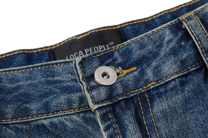 Close-up of the blue denim waistband showing a metal button, golden stitching, belt loop, and inner label
