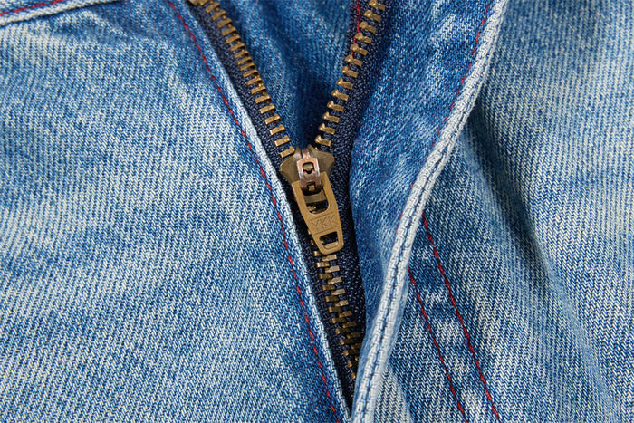 Close-up of the jeans zipper fly with brass-colored teeth and red-stitched denim seams