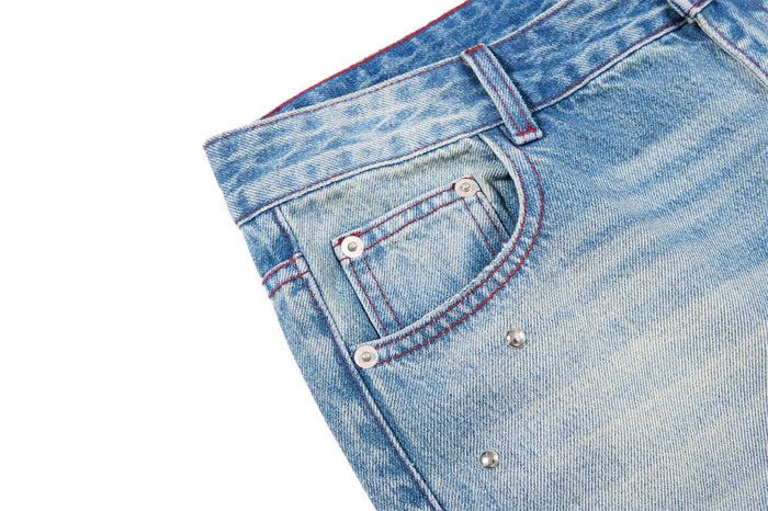 Close-up of a front pocket with red stitching and silver stud details on washed blue denim