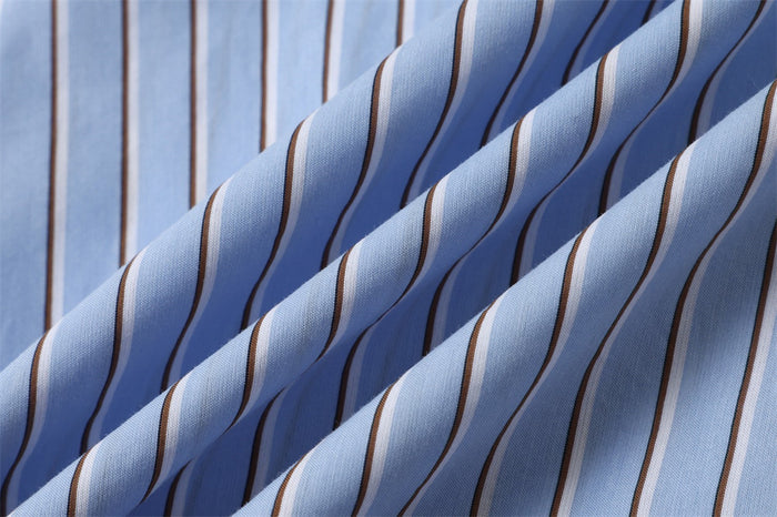 Close-up of light blue shirt fabric showing raised folds and alternating narrow vertical stripes