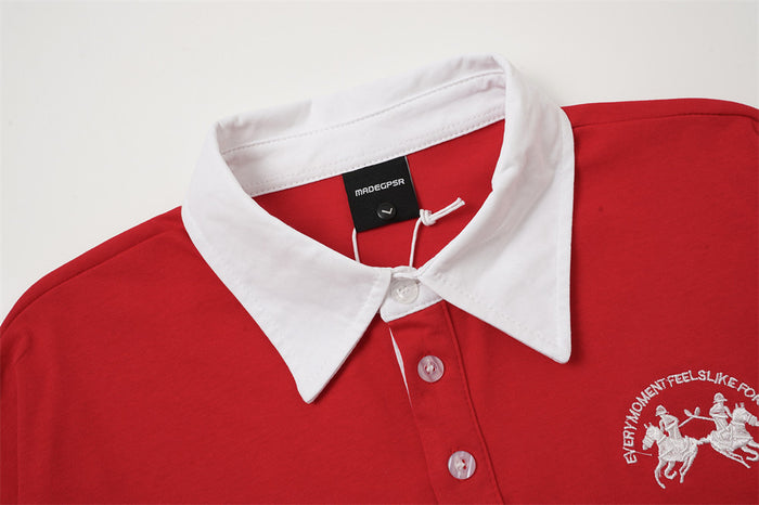 Close-up of the red rugby polo shirt showing its white pointed collar, button placket, and embroidered chest crest