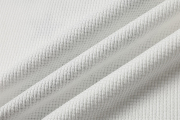 Close-up of white waffle-knit shirt fabric showing its raised grid texture and soft folds