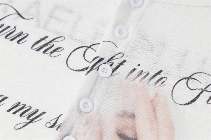 Close-up of black cursive lettering, white buttons, and part of the face graphic on the shirt