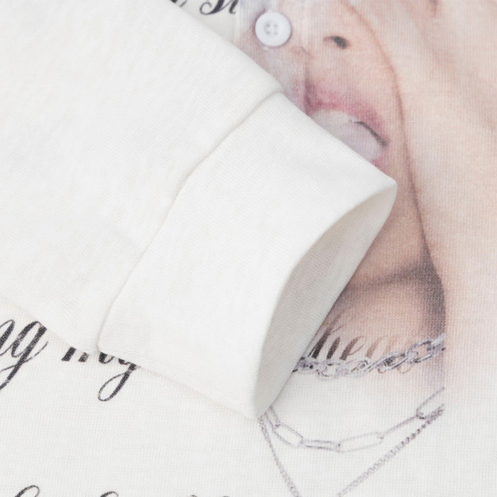Close-up of a white sleeve cuff layered over the shirt’s printed face and necklace graphic