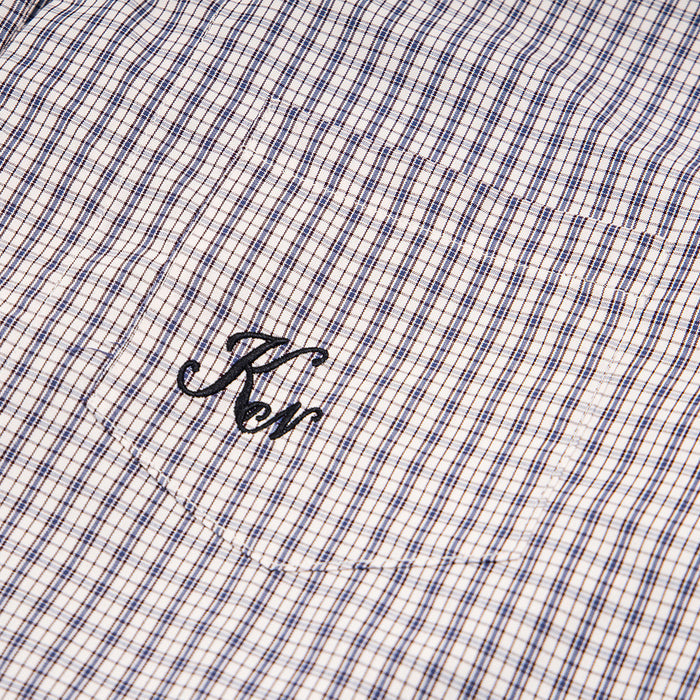 Close-up of the light beige plaid shirt chest pocket with black embroidered lettering