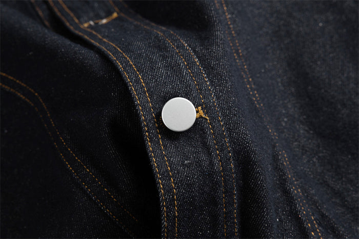 Close-up of a silver snap button on the dark denim placket with gold stitching