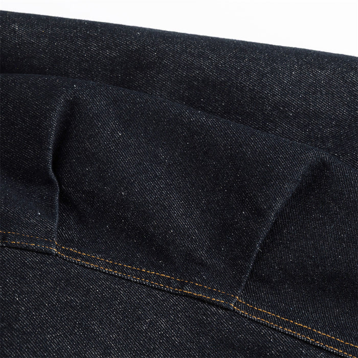 Close-up of a dark denim jacket panel showing a folded seam and contrasting gold stitching