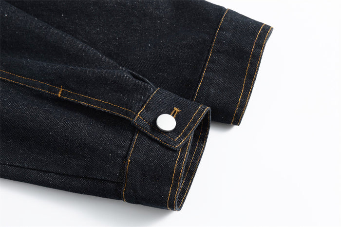 Close-up of a dark denim sleeve cuff with a silver snap and reinforced gold stitching