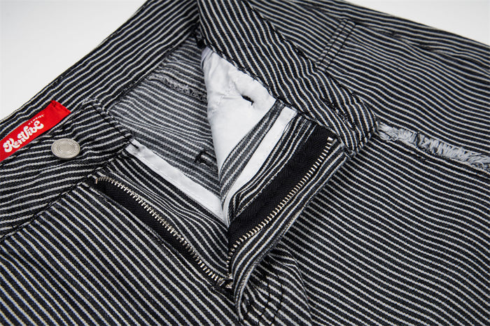 Open zipper fly and metal button detail on black and white striped jeans, showing the inner waistband