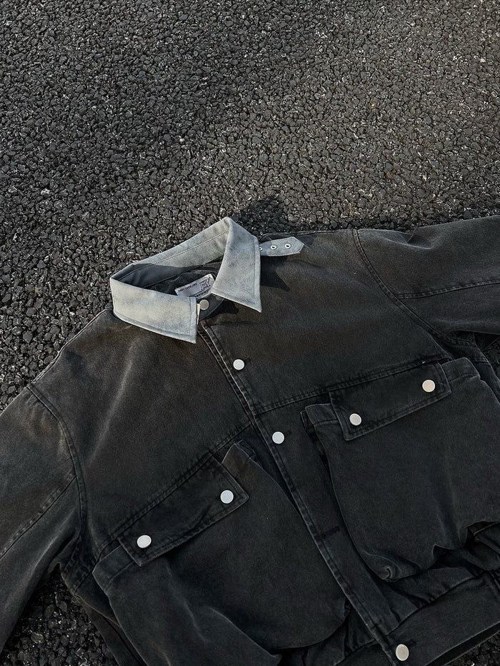 Close-up of the black bomber jacket front showing its buckle collar, snap closure, and flap cargo pockets