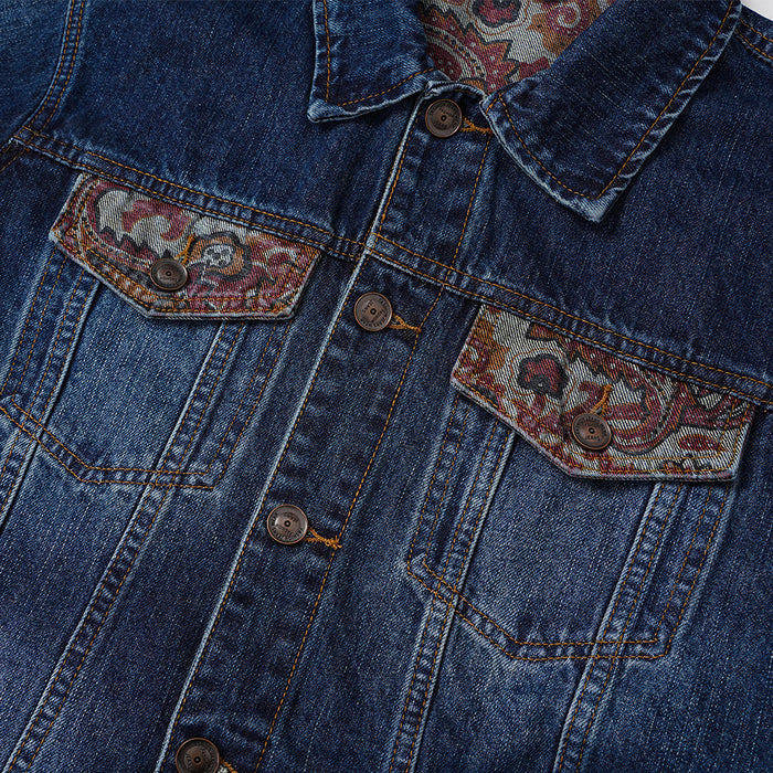 Front chest detail of a washed denim jacket with two paisley jacquard flap pockets and metal buttons