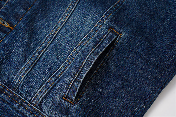 Close-up of a dark blue denim jacket side welt pocket with contrasting double stitching