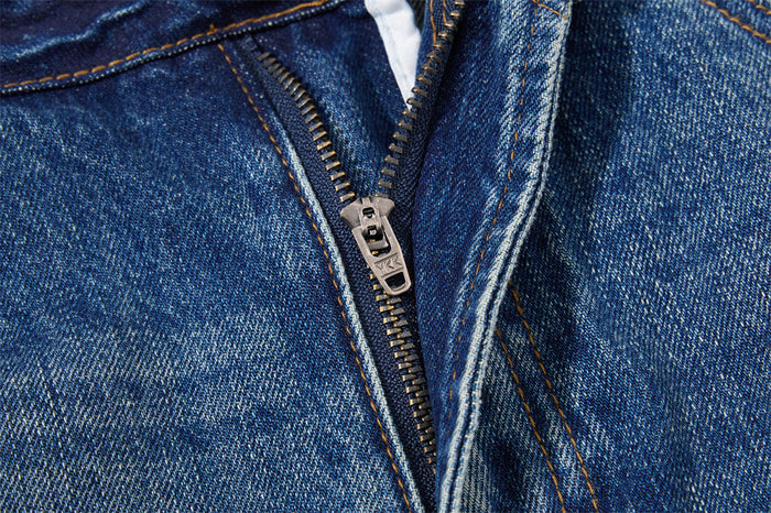 Close-up of the metal zipper fly and textured blue denim with contrasting tan stitching