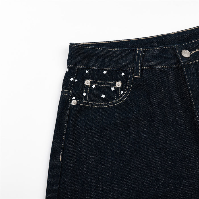 Close-up of a dark indigo jeans front pocket decorated with white stars, rivets, and contrast stitching