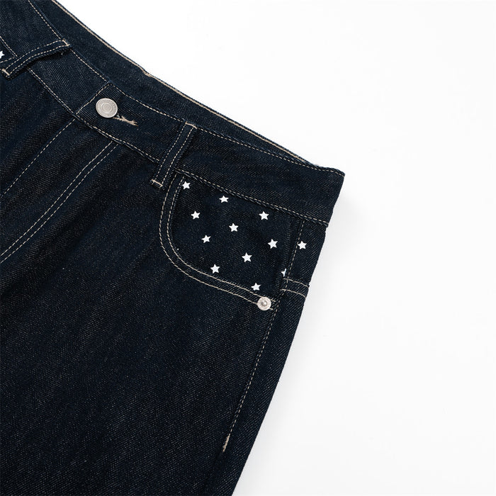 Detail of a dark indigo jeans front pocket with white star pattern, rivets, belt loop, and contrast stitching