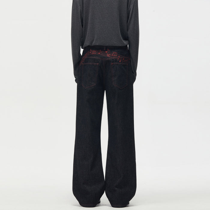 Men's black wide-leg raw denim jeans with red music note embroidery on back waistband, straight fit full-length view