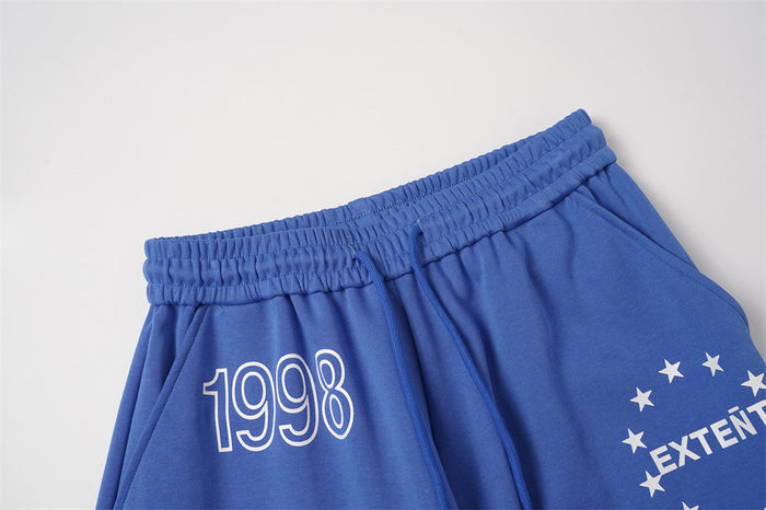 Close-up of blue sweatpants waistband, drawstring, 1998 print, and partial star graphic