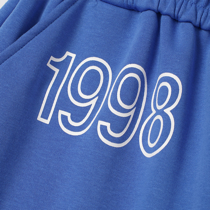 Close-up of white outlined 1998 lettering printed on blue sweatpants fabric