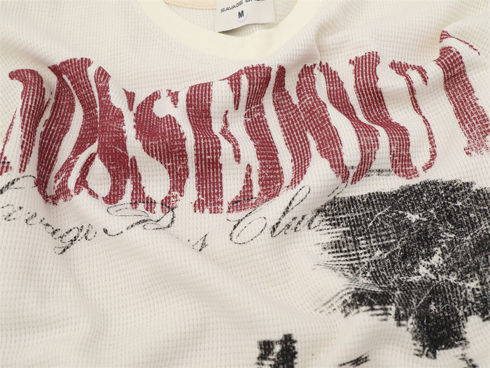 Close-up of cream waffle-knit fabric with distressed red lettering, script text, and portrait graphic