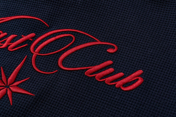 Close-up of red embroidered Nast Club lettering on the textured navy waffle-knit fabric