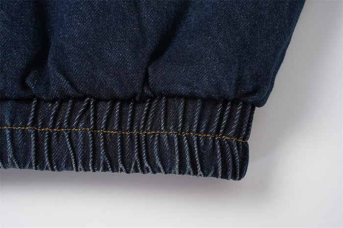 Close-up of the dark denim jacket's gathered elastic hem with contrasting yellow stitching
