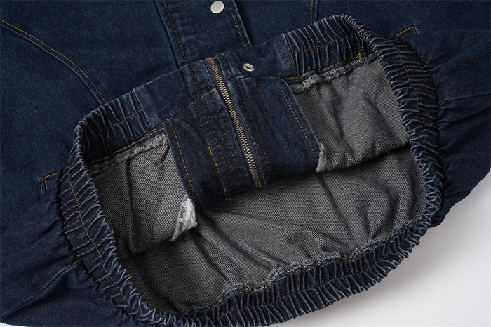 Inside view of the denim jacket hem showing gray lining, folded waistband, zipper, and gathered elastic edges