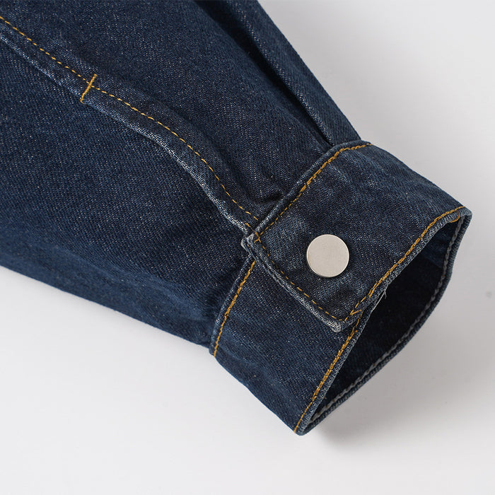 Close-up of the dark denim jacket sleeve cuff with yellow stitching and a round snap button