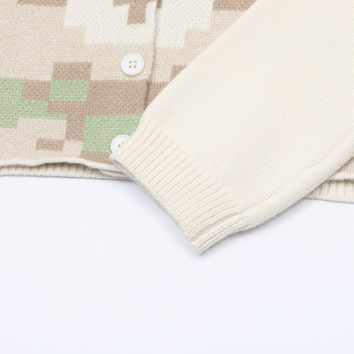 Close-up of the cream cardigan showing its ribbed sleeve cuff, knitted hem, and lower pixel pattern
