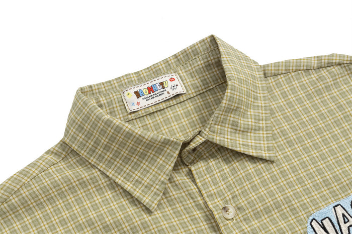 Close-up of the olive plaid shirt collar, button placket, and sewn neck label