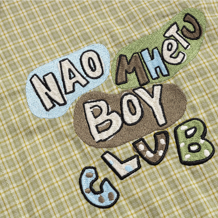 Close-up of colorful raised embroidered lettering reading Nao Mhen Boy Club on olive plaid fabric