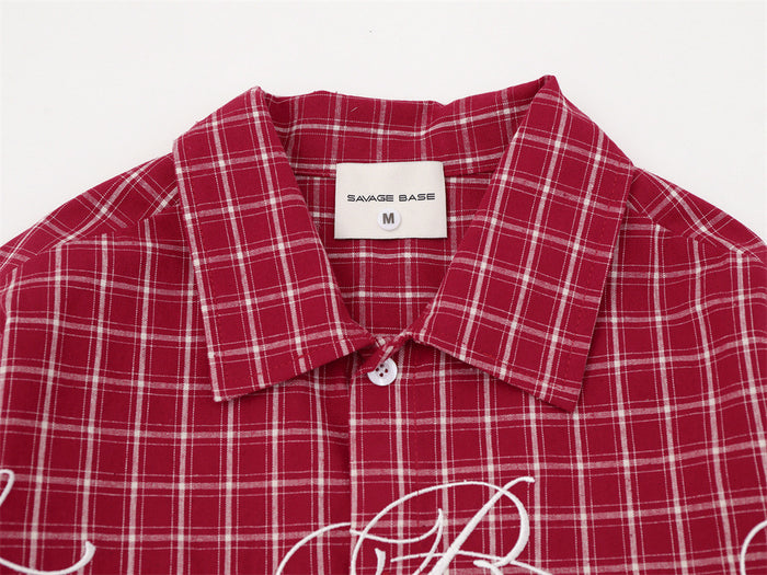 Close-up of the red plaid shirt collar, inner label, top button, and partial white cursive embroidery