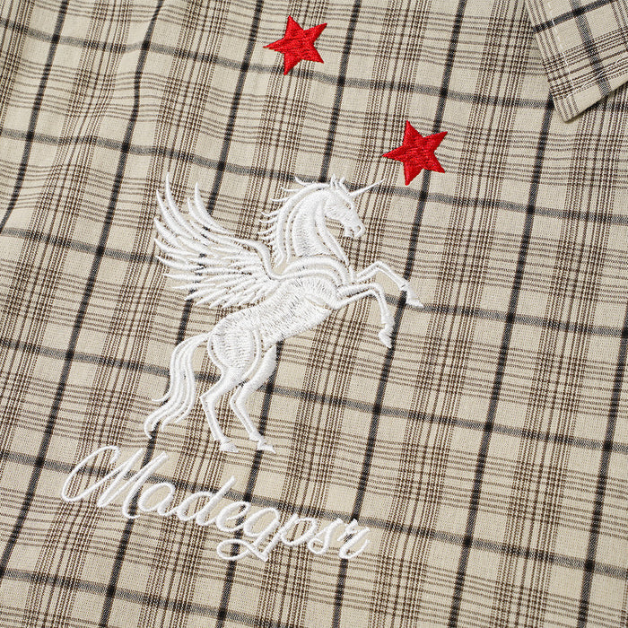 Close-up of white winged horse embroidery with red stars on the beige plaid shirt front