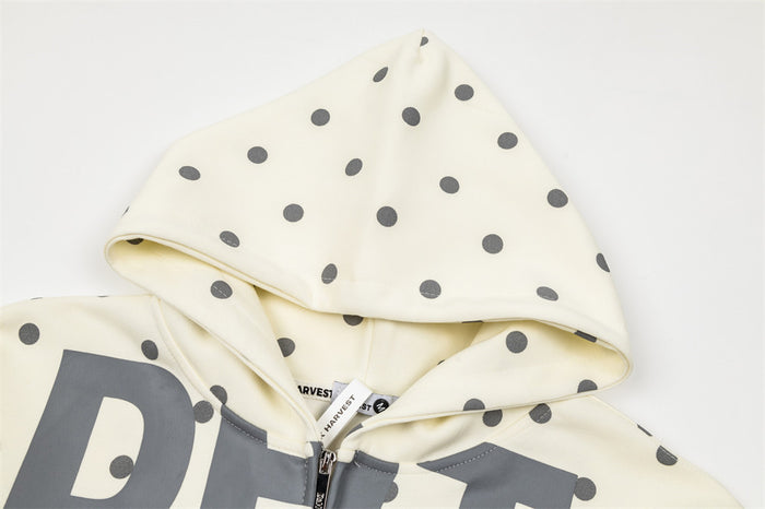 Close-up of the cream polka dot hoodie hood, drawstrings, zipper, and printed front graphic