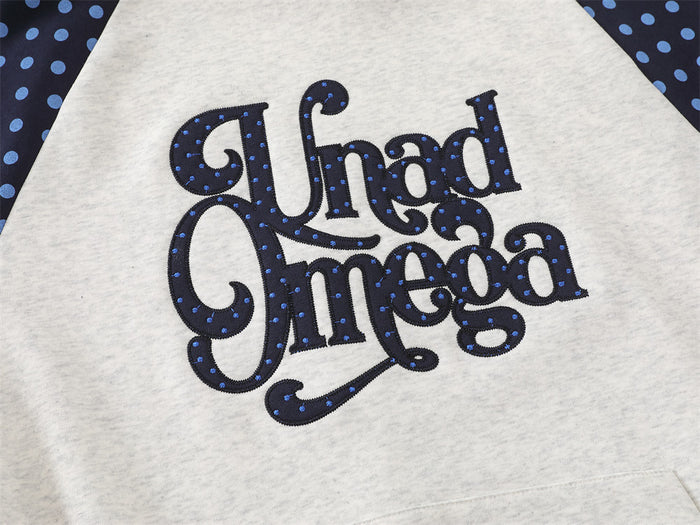 Close-up of ornate dark lettering with blue dot accents on the light gray hoodie front