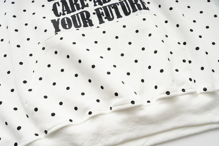 Close-up of the cream hoodie body and ribbed lower hem, with black polka dots and partial front text visible