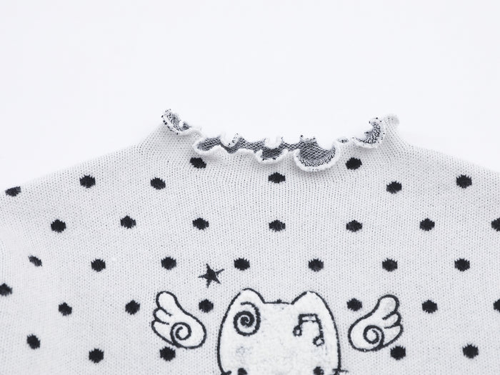 Close-up of white knit fabric with black polka dots, ruffled mock neck, and cat graphic