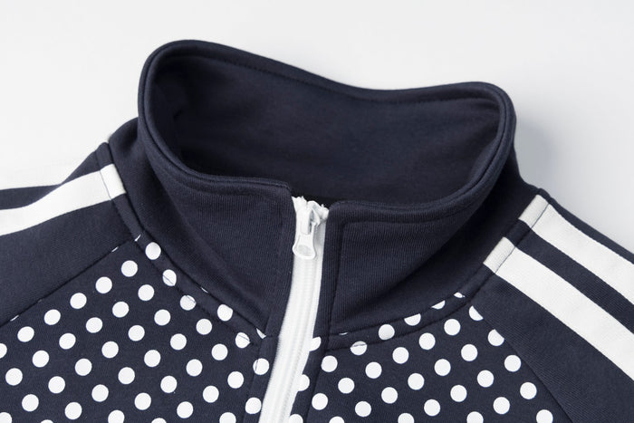 Close-up of navy stand collar, white zipper and striped shoulder detail on a polka-dot jacket