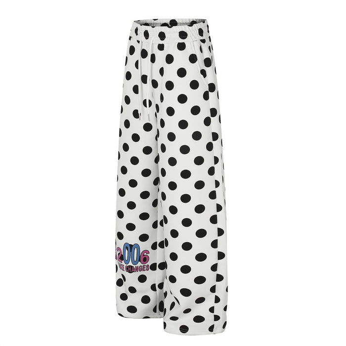 Angled view of white oversized wide-leg pants covered in black polka dots with a colorful graphic near the hem