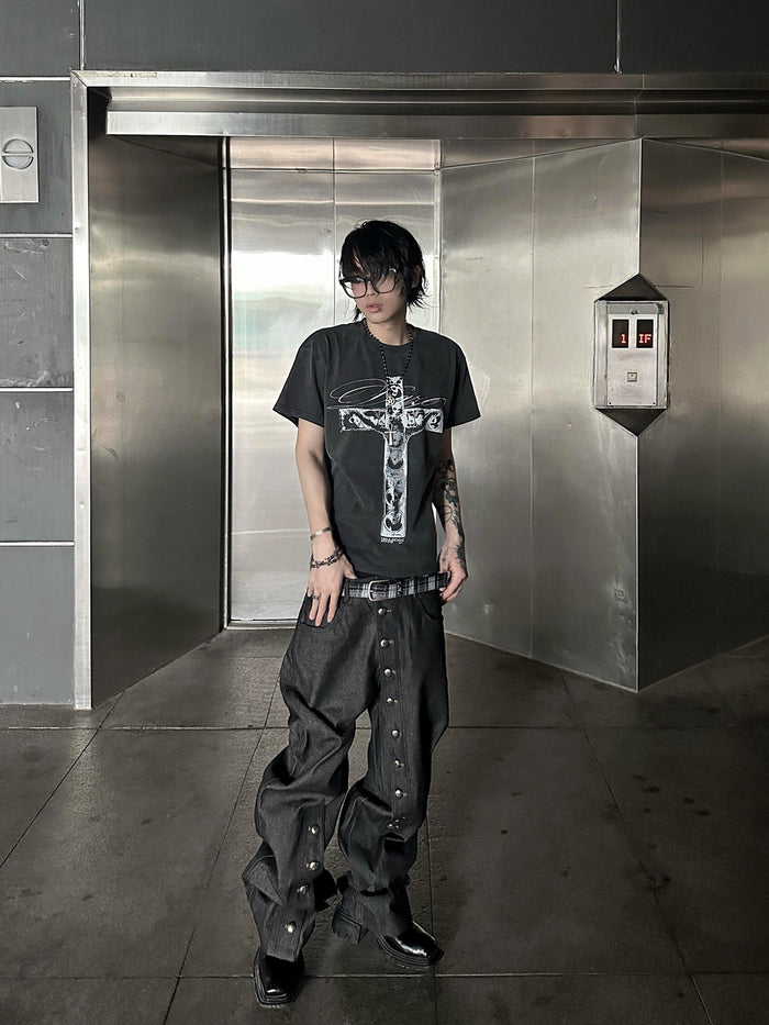 Raw black denim straight-leg jeans with full-length side metal snap buttons, worn with a graphic tee and platform boots