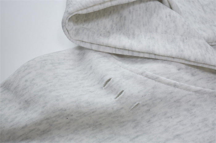 Close-up of light gray hoodie fabric showing the hood edge and small distressed slits on the body