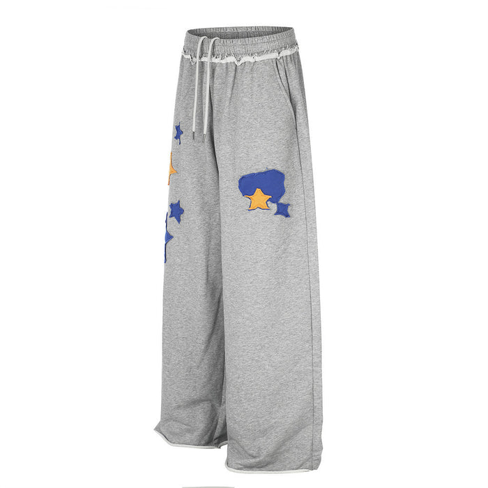 Angled front view of gray wide-leg sweatpants with blue and orange star appliqués on the leg