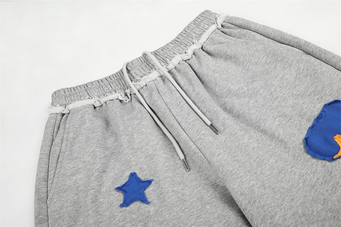 Close-up of gray sweatpants waistband with drawstring, elastic trim, and blue star appliqué details