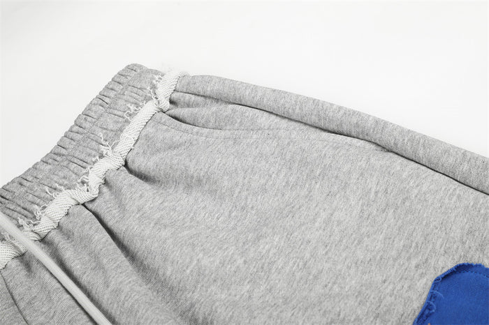 Close-up of gray sweatpants elastic waistband and side pocket opening with a blue appliqué partially visible