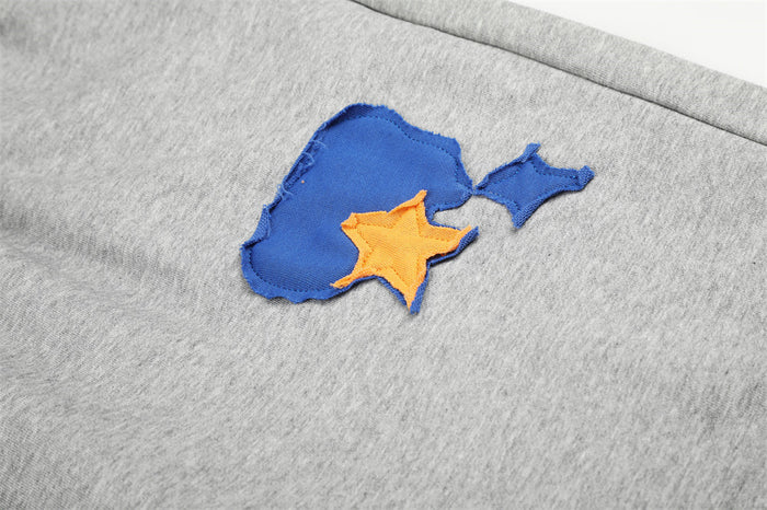 Close-up of layered blue and orange star appliqué stitched onto gray sweatpants fabric